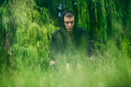 Portrait of a sad, crouching man in a black hoodieの写真素材