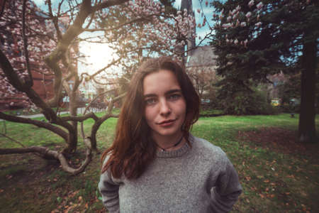 Portrait of a young, smiling woman in a park in front of a magnolia treeの写真素材
