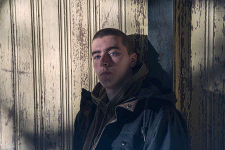 portrait of a serious young man leaning against an old wooden wallの写真素材