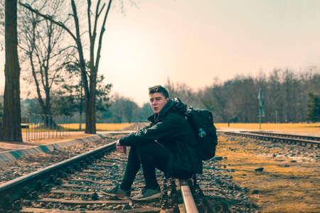 happy young man with backpack sitting on railroad tracksの写真素材