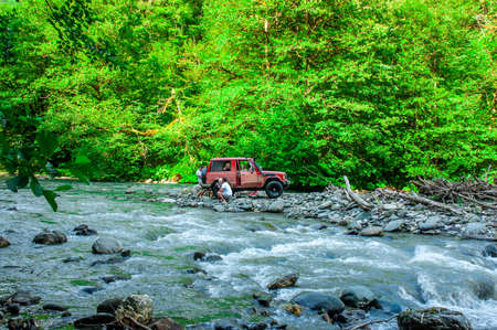 People crossing the river on the red car with children. Mzimta riverのeditorial素材