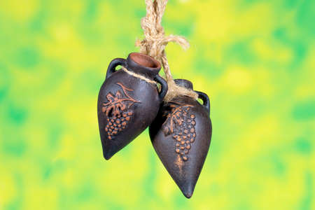 Handmade clay jugs  with grape pattern with ropes attached on green background.の写真素材