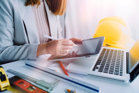 Two colleagues discussing data working and tablet, laptop with on on architectural project at construction site at desk in officeの写真素材