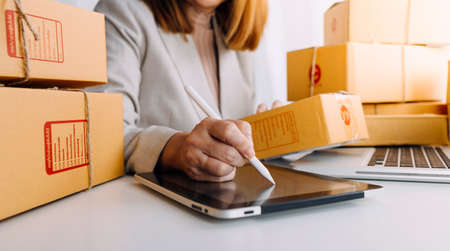 Young woman small business owner online shopping at home. taking note of orders from customers with mobile phones. SME entrepreneur or freelance life style concept.の写真素材