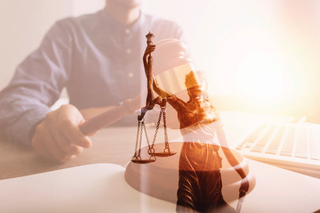 Justice and law concept.Male judge in a courtroom with the gavel, working with, computer and docking keyboard, eyeglasses, on table in morning lightの写真素材