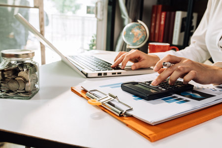 Woman entrepreneur using a calculator with a pen in her hand, calculating financial expense at home officeの写真素材