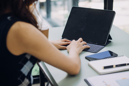 Young business woman sitting in office at table and using smartphone. On desk is laptop and tablet...