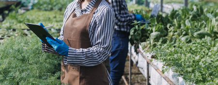 female farmer working early on farm holding wood basket of fresh vegetables and tabletの写真素材