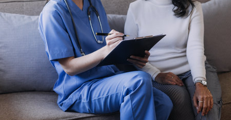 Homecare nursing service and elderly people cardiology healthcare. Close up of young hispanic female doctor nurse check mature caucasian man patient heartbeat using stethoscope during visitの写真素材