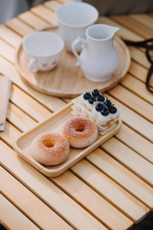 Young pretty brunette twin girls sitting on the grass with legs slightly bent in knees and looking in a brown book, wearing casual coat in autumn sunny weather on blurry background.の写真素材