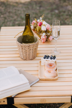 Young pretty brunette twin girls sitting on the grass with legs slightly bent in knees and looking in a brown book, wearing casual coat in autumn sunny weather on blurry background.の写真素材