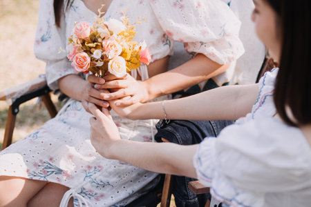 Young pretty brunette twin girls sitting on the grass with legs slightly bent in knees and looking in a brown book, wearing casual coat in autumn sunny weather on blurry background.の写真素材