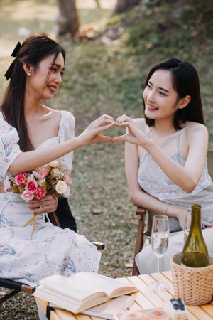 Young pretty brunette twin girls sitting on the grass with legs slightly bent in knees and looking in a brown book, wearing casual coat in autumn sunny weather on blurry background.の写真素材