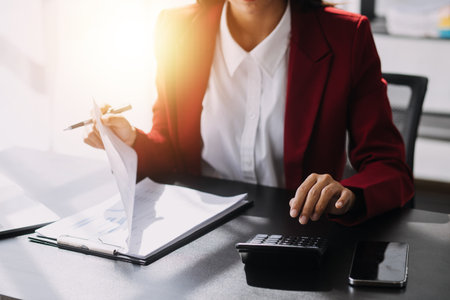 Asian Business woman using calculator and laptop for doing math finance on an office desk, tax, report, accounting, statistics, and analytical research conceptの写真素材