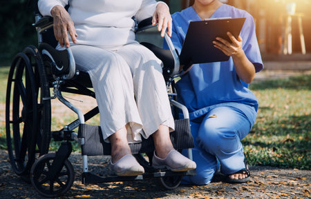 Asian young caregiver nurse support senior older male walking outdoors. Specialist girl doctor help and take care of elderly mature man patient doing physical therapy in public park at nursing home.の写真素材