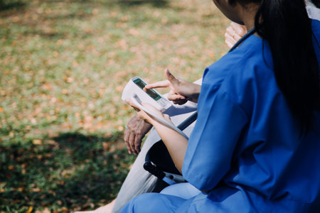 Asian young caregiver nurse support senior older male walking outdoors. Specialist girl doctor help and take care of elderly mature man patient doing physical therapy in public park at nursing home.の写真素材