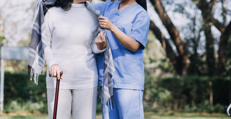 Asian young caregiver nurse support senior older male walking outdoors. Specialist girl doctor help and take care of elderly mature man patient doing physical therapy in public park at nursing home.の写真素材