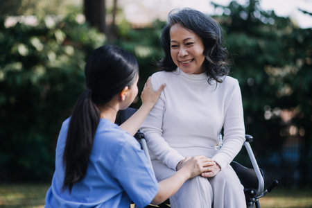 Asian young caregiver nurse support senior older male walking outdoors. Specialist girl doctor help and take care of elderly mature man patient doing physical therapy in public park at nursing home.の写真素材