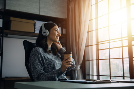 Young adult happy smiling Hispanic Asian student wearing headphones talking on online chat meeting using laptop in university campus or at virtual office. College female student learning remotely.の写真素材