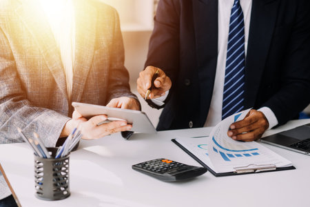Financial analysts analyze business financial reports on a digital tablet planning investment project during a discussion at a meeting of corporate showing the results of their successful teamwork.の写真素材