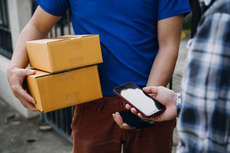 Delivery man with protective mask and gloves delivering parcels during lockdown and pandemic and holding mobile contactless payment machineの写真素材