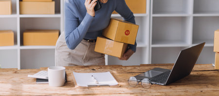 Startup SME small business entrepreneur of freelance Asian woman wearing apron using laptop and box to receive and review orders online to prepare to pack sell to customers, online sme business ideas.の写真素材