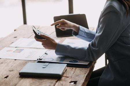 Attractive smiling young asian business woman work at home office, Asian woman working on laptop computer holding tablet.の写真素材