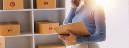 Startup SME small business entrepreneur of freelance Asian woman using a laptop with box Cheerful success Asian woman her hand lifts up online marketing packaging box and delivery SME idea conceptの写真素材