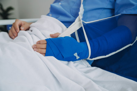 Man with broken arm in cast lying on bed in hospital. The emergency center treatment is plaster and hangs with sling for a further cure in an orthopedic clinic. Patient pain from accident injury.の写真素材