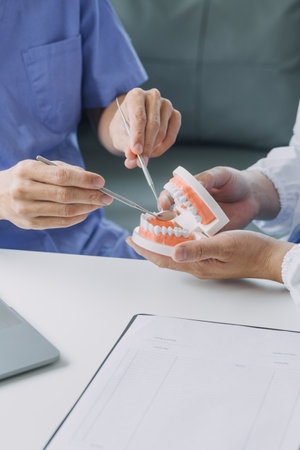 Male dentist with plastic jaw model on light background