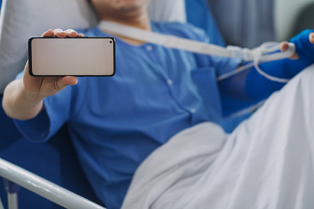 Man with broken arm in cast lying on bed in hospital. The emergency center treatment is plaster and hangs with sling for a further cure in an orthopedic clinic. Patient pain from accident injury.の写真素材