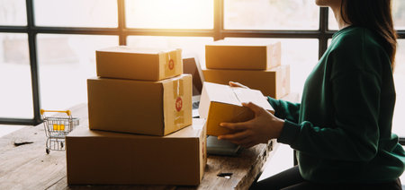 SME entrepreneur Small business entrepreneurs Online selling ideas,Happy Young Asian business owner work on computer and a boxs at home,delivery SME procurement package box deliver to customers,の写真素材