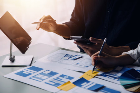 Close up ux developer and ui designer brainstorming about mobile app interface wireframe design on table with customer breif and color code at modern office.Creative digital development agencyの写真素材