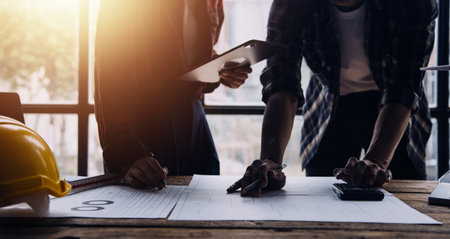 Three colleagues discussing data working and tablet, laptop with on on architectural project at construction site at desk in officeの写真素材