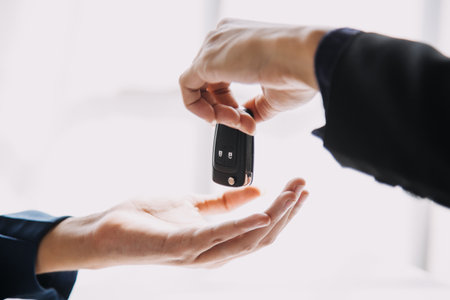 Closeup of Asian female signing car insurance document or lease paper contract or agreement. Buying or selling new or used vehicle with car keys on table.の写真素材