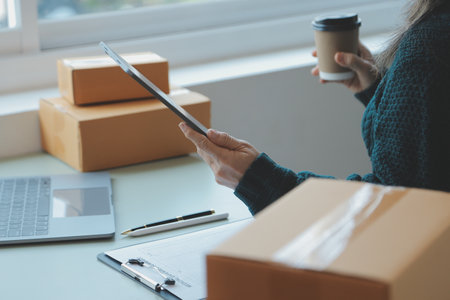Startup SME small business entrepreneur of freelance Asian woman wearing apron using laptop and box to receive and review orders online to prepare to pack sell to customers, online sme business ideas.の写真素材