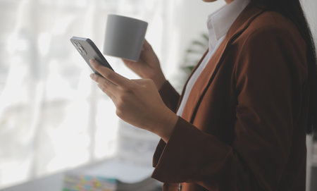 Attractive smiling young asian business woman work at home office, Asian woman working on laptop computer holding tablet.の写真素材