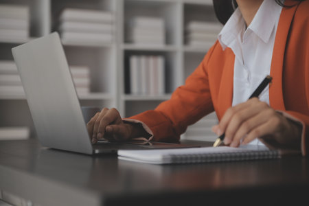 Attractive smiling young asian business woman work at home office, Asian woman working on laptop computer holding tablet.の写真素材