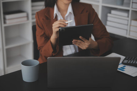 Attractive smiling young asian business woman work at home office, Asian woman working on laptop computer holding tablet.の写真素材