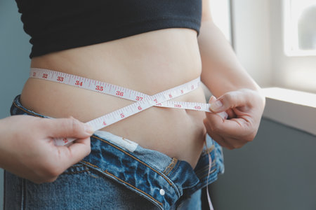 Close up of a belly with scar from c-section and abdominal fat. Women's health. A woman dressed up in sportswear demonstrating her imperfect body after a childbirth with nursery on the background.の写真素材