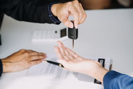 A car rental company employee is handing out the car keys to the renter after discussing the rental details and conditions together with the renter signing a car rental agreement. Concept car rental.の写真素材