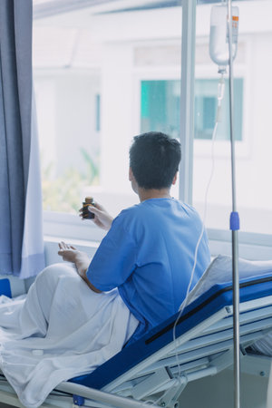 Asian male patient lying on bed with face mask in recovery room in hospital ward. All people wearing mask to prevent covid19 virus infection during coronavirus pandemic. The man feels lonely and bore.の写真素材