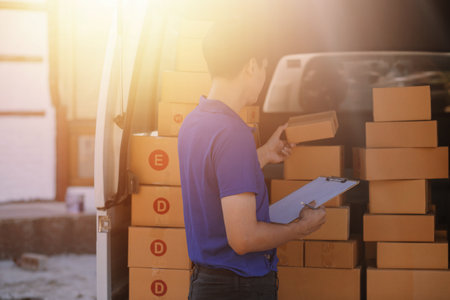 Delivery man with cardboard box checking document list In van and parcels on seat outside the...