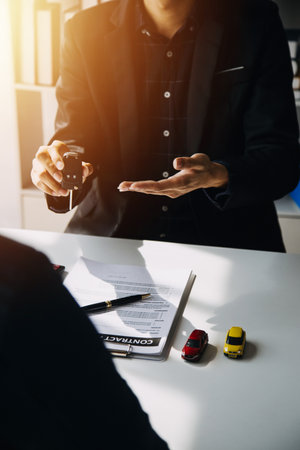 Hand holding car keys and car rental concept A close-up view of the agent, giving the customer the car keys after signing the lease, rental form and car name.の写真素材