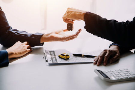 A car rental company employee is handing out the car keys to the renter after discussing the rental details and conditions together with the renter signing a car rental agreement. Concept car rental.の写真素材