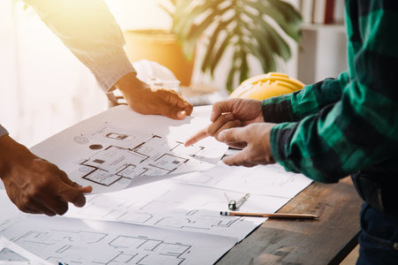 Three colleagues discussing data working and tablet, laptop with on on architectural project at construction site at desk in officeの写真素材