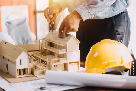 Three colleagues discussing data working and tablet, laptop with on on architectural project at construction site at desk in officeの写真素材