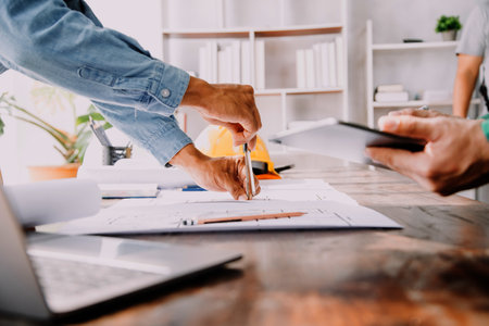 Three colleagues discussing data working and tablet, laptop with on on architectural project at construction site at desk in officeの写真素材