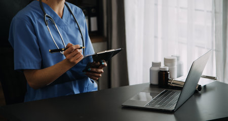 Doctor working with laptop computer and writing on paperwork. Hospital background.の写真素材