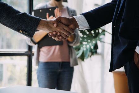 Image of business partners handshaking over business objects on workplace